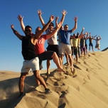 Group of people enjoying and posing with raised arms on a sand dune.